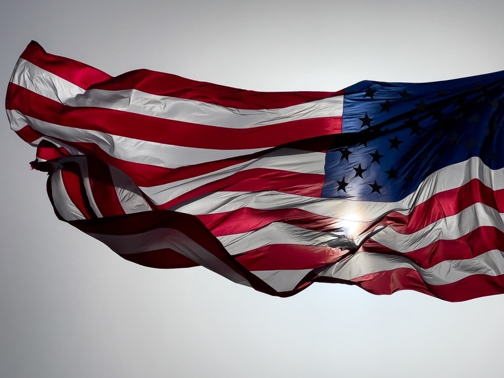 American flag waving in the wind with sun shining through.